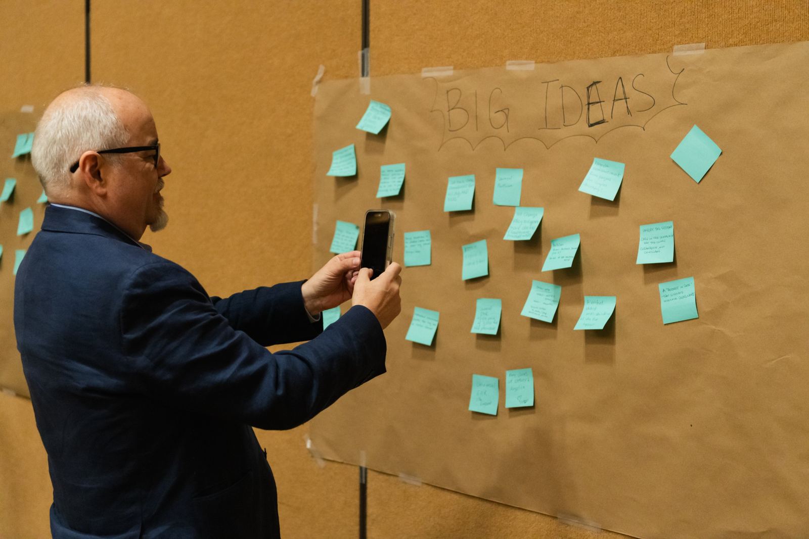 An attendee photographs the Big Ideas wall, covered in blue sticky notes